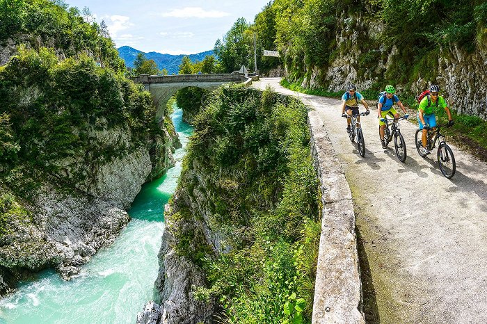 Drei Radfahrer fahren an der Napoleon-Brücke in der Nähe von Kobarid vorbei