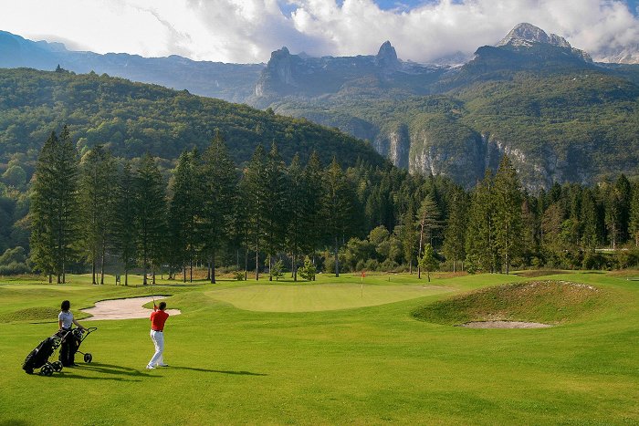 Par igra golf na zelenici obdani s hribi