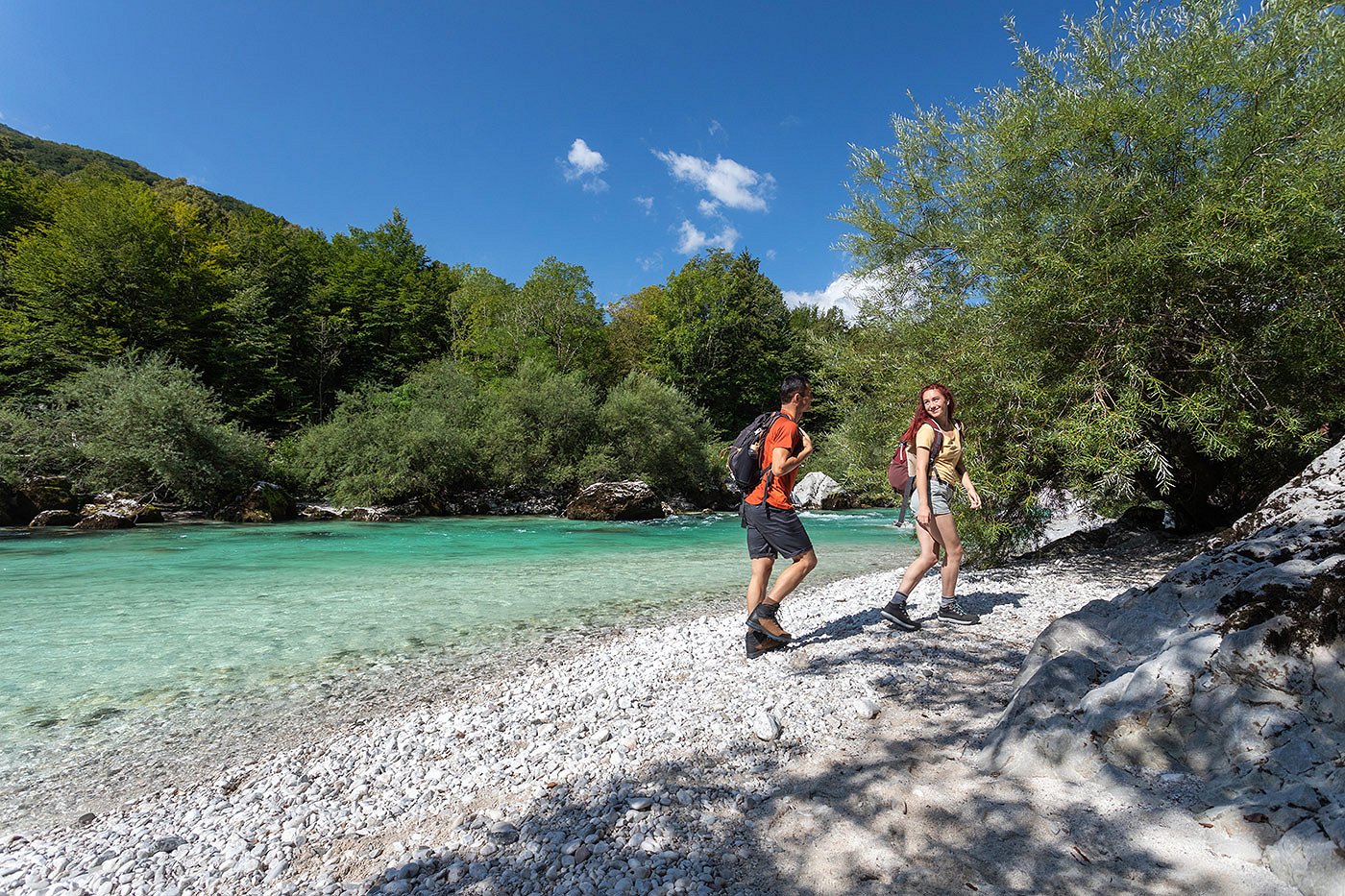 The hikers are walking along the sandy bank of the Soča River