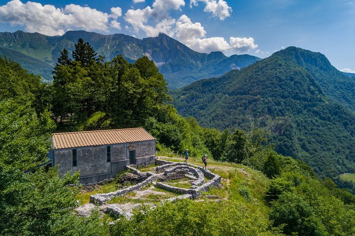 Gli escursionisti camminano tra le rovine, sullo sfondo il monte Krn