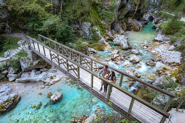 The family enjoys the views from the wooden bridge that crosses the green-blue Tolminka river.
