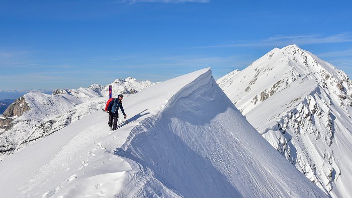 Lo sciatore alpinista gode della vista dalla cima di una montagna innevata